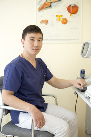 Asian male ophthalmologist is at his workplace working with the deviceの写真素材