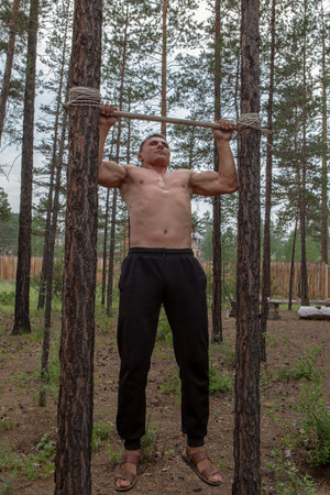 The athlete does push-ups on a makeshift bar between trees in a summer cottage