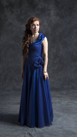 Young woman in a dark blue classic evening dress posing in the studio on a gray background.の写真素材