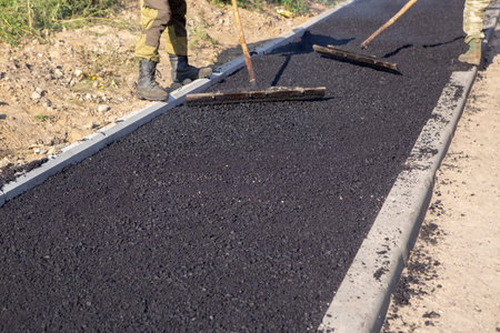 On the sidewalk, road workers leveling freshly laid hot asphalt