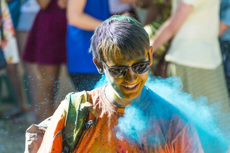 Lviv, Ukraine - August 28, 2016: Cheerful young man with glasses in blue powder  during the festival of color in a city park in Lviv.のeditorial素材