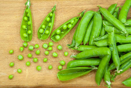 Fresh pods of sweet green peas in basket, on wooden boardの写真素材