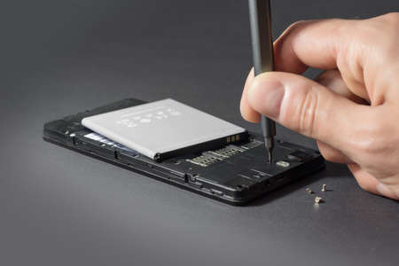Human Hand Repairing Cellphone With Screwdriver On Desk.の写真素材