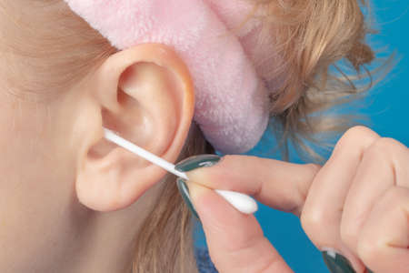Female cleaning ear with cotton bud on blue background.の写真素材