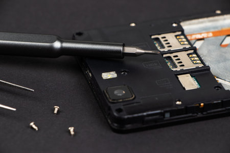 Broken mobile phone and repair tools on dark background, flat layの写真素材