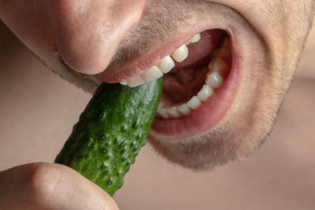 Vertarianism. A man bites a cucumber. Photo of a vegetarian biting a cucumberの写真素材