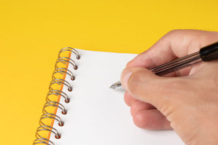 Men hand with pen over paper isolated on yellow background.