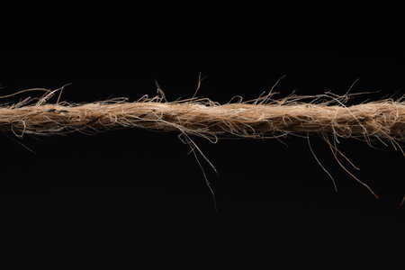 Long rough brown rope on black background.