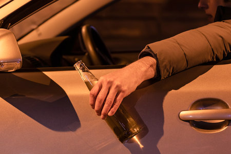 Drunk man driving a car with a bottle of beer at the night. Don't drink and drive concept.の写真素材