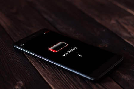 Energy concept: smartphone with low battery on wooden background. All screen graphics are made upの写真素材