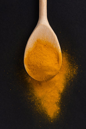 Turmeric powder in the wooden spoon on dark background.