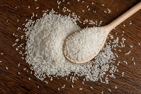 White rice in a wooden spoon, scattered rice on a wooden background.の写真素材
