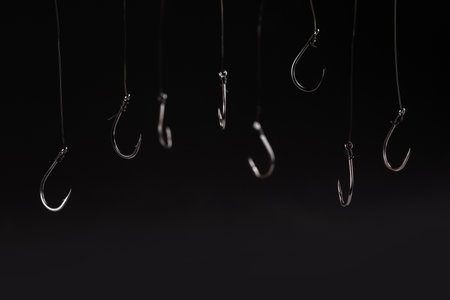 A fishing hook hanging on a fishing line on a black background. conceptの写真素材