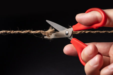 Worn rope ready to break, with scissors on black background.の写真素材