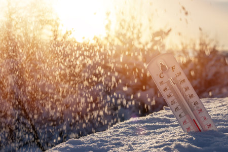 Thermometer on snow shows low temperatures in celsius or farenheit. On the Sunset.の写真素材