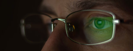 Close up view of man wears computer glasses for reducing eye strain blurred vision looking at pc screen with computer reflection using internet, reading, watching, working online.の写真素材
