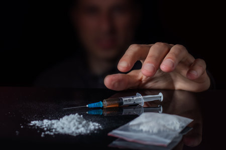 The concept of anti drugs. Drug addict reaches for another dose of the drug in the syringe. Guy addicted, male drug addict, drug syringeの写真素材