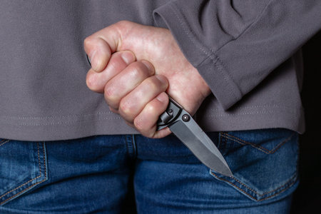 Criminal with knife weapon hidden behind his back.