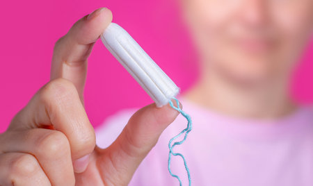 Young woman holding menstruation tampon in hand - women's menstrual cramps. Menstruation, means of...