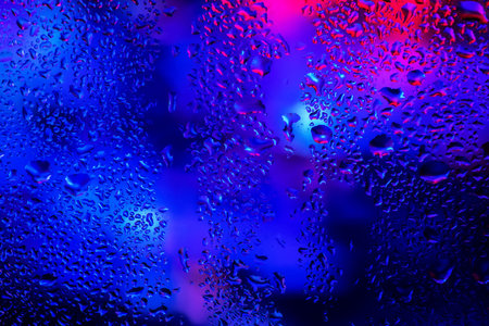 Rain drops and condensation on the window glass against the background of the neon light.