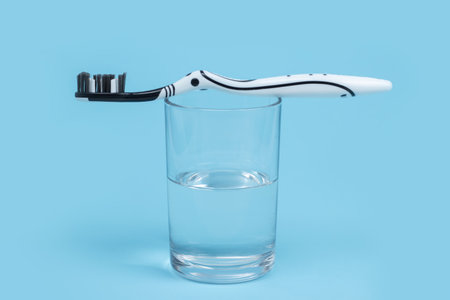 A black and white toothbrush on a glass with mouthwash on blue background with copy spaceの写真素材