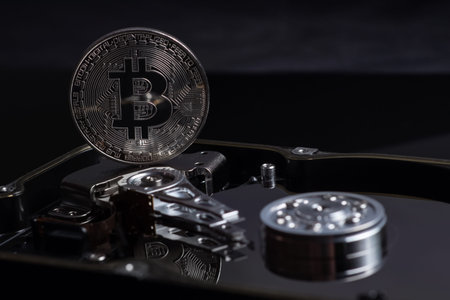 Silver Bitcoin coin on the opened HDD disk. Electronic money, cryptocurrency.