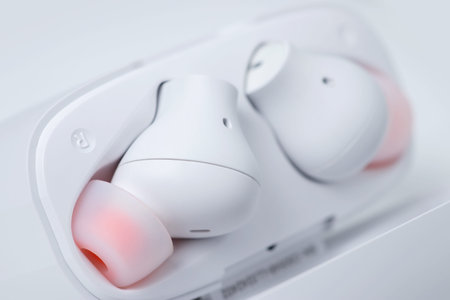 Two white wireless headphones in a case on a white background,