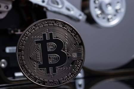 Silver Bitcoin coin on the opened HDD disk. Electronic money, cryptocurrency.