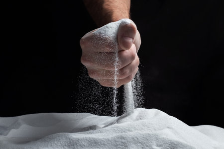 Man with handful of white dry sand in her hands, spilling sand through fingers on black background. Concept of flow of life. Close up of grains of pure natural mineral quartz.の写真素材