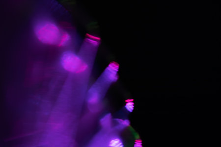 Blur neon light. Lens flare overlay. Bokeh fluorescent flash gleam. Defocused blue purple color flecks on dark black abstract background.の写真素材