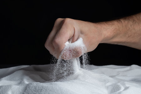 Man with a handful of white dry sand in her hands, spilling sand through fingers on black background. Concept of flow of life. Close up of grains of pure natural mineral quartz.の写真素材