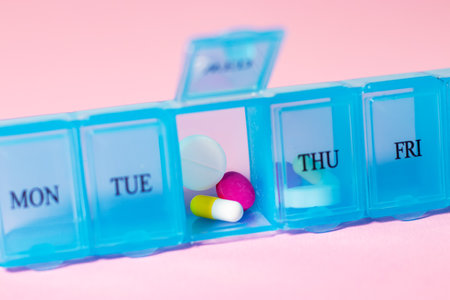 Pill organizer with variety of pills and supplement. Weekly Pill Organizer on pink background. Daily pill box with medications and nutritional supplements.の写真素材