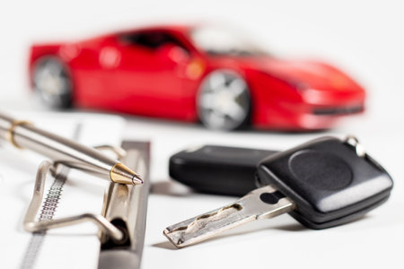 Car insurance form, pen and key on wooden table, and red car background.の写真素材