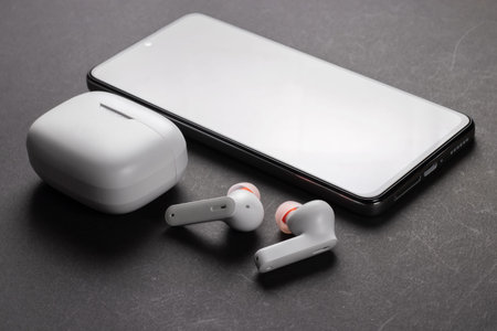 Wirelsss white headphones with case and smartphone on dark background.