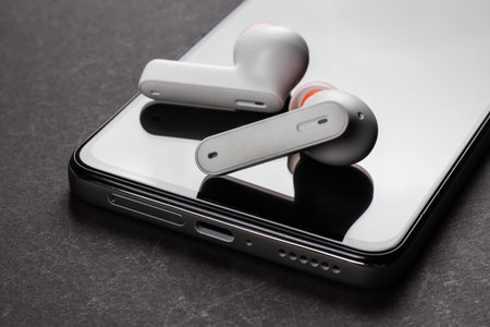 Wirelsss white headphones and smartphone on dark background.