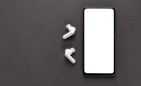 Mobile phone with empty screen and earphones on black surface. Wireless earphones, mobile phone on...
