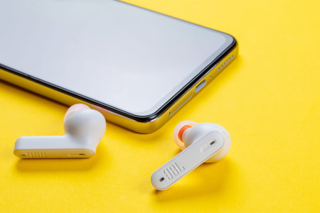 Dnipo, Ukraine, February 20, 2023: JBL Tune 230 NC TWS headphones. Closeup modern headphone and smartphone on yellow background.のeditorial素材