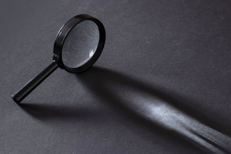 Closeup of magnifying glass standing on dark surface with beam of light.の写真素材