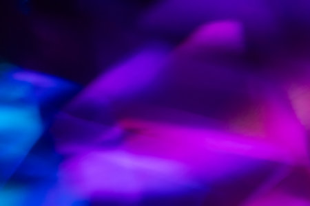 Blur neon light. Lens flare overlay. Bokeh fluorescent flash gleam. Defocused blue purple color flecks on dark black abstract background.の写真素材