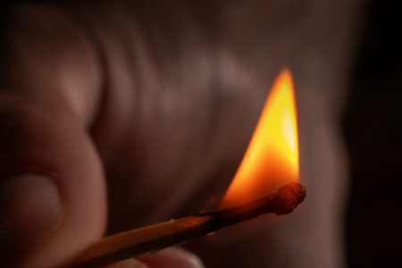 Hand holding burning match stick. Photo on a black background.