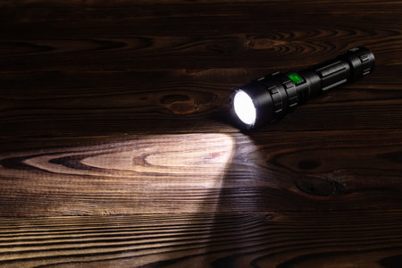 Flashlight and a beam of light in darkness. A modern led lamp with bright projection on dark wood table. Surface with copy space.の写真素材