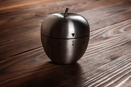 Metal apple kitchen timer on wooden background.