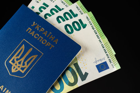 Ukrainian passport and 100 euro banknotes on black background.