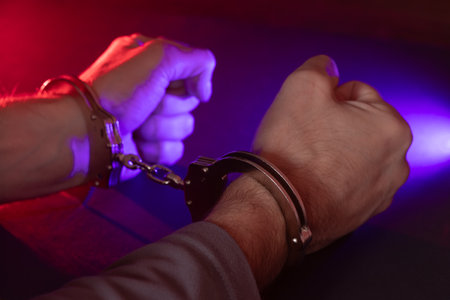 Male hand in handcuffs at night with police car lights.の写真素材