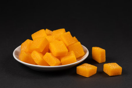 Dried and candied mango cubes on the white plate. Side view, close up, selective focus, food concept.の写真素材