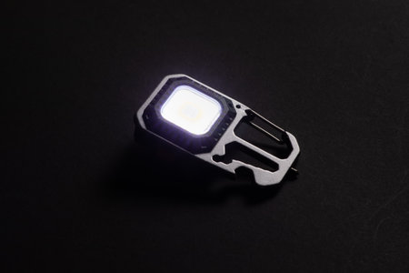 LED Flashlight Keychain and a beam of light in darkness. A modern led lamp with bright projection on dark tableの写真素材