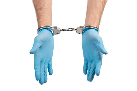 male hands in handcuffs and medical glove on white background, concept of medical corruption, bribery, crimeの写真素材