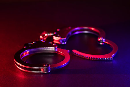 Police raid at night and you are under arrest concept. Silhouette of handcuffs. Image with the flashing red and blue police lights dark background.の写真素材