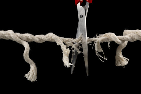 Worn rope ready to break, with scissors on black backgroundの写真素材