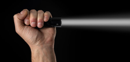 Black flashlight in human hands on a black background, including a white beam.の写真素材
